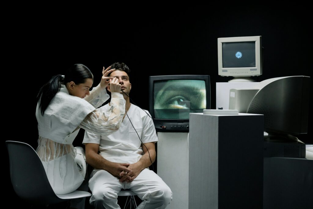 A woman performs an eye examination on a man in a vintage tech lab.